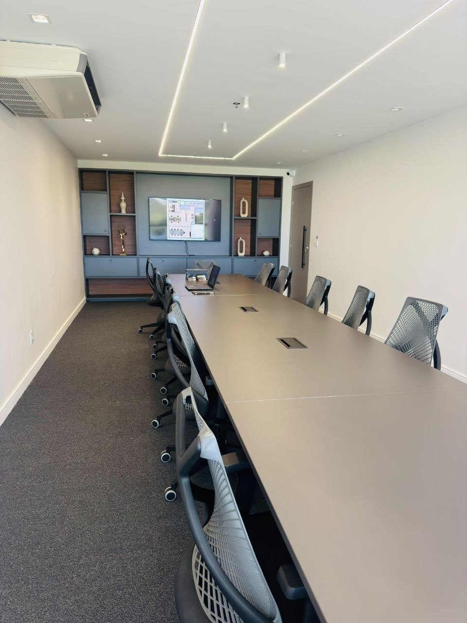Sala corporativa com mesa longa, cadeiras ergonômicas e painel ao fundo