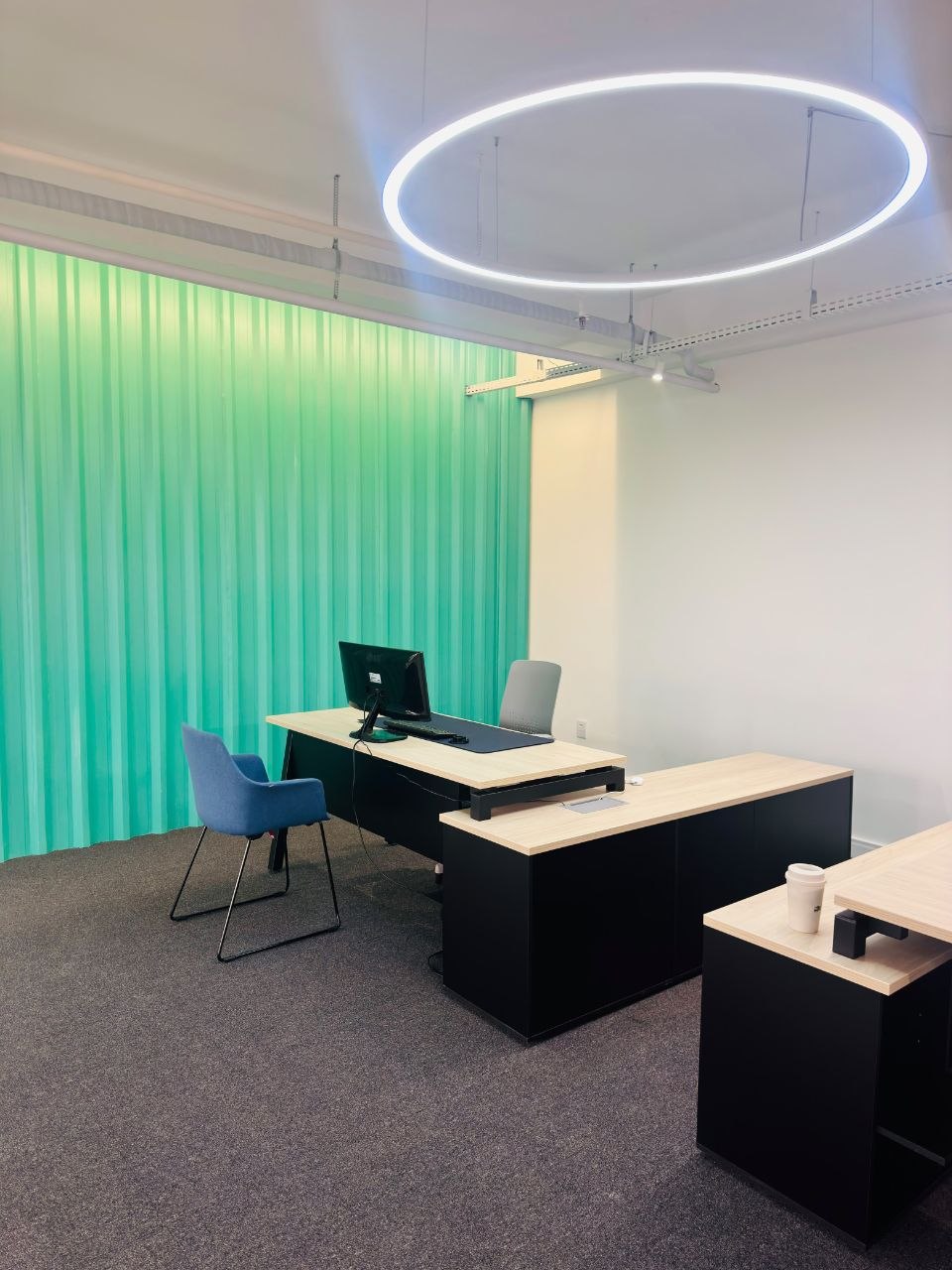 Sala de atendimento com mesa corporativa, cadeira azul e cortina verde